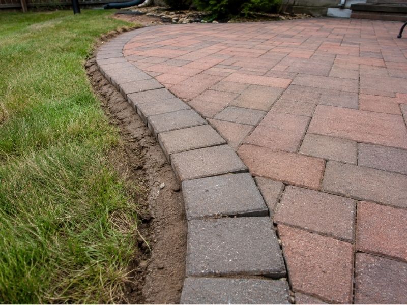Brick patio with secure edge restraints preventing pavers from spreading into the lawn in a residential backyard in Frisco, TX.