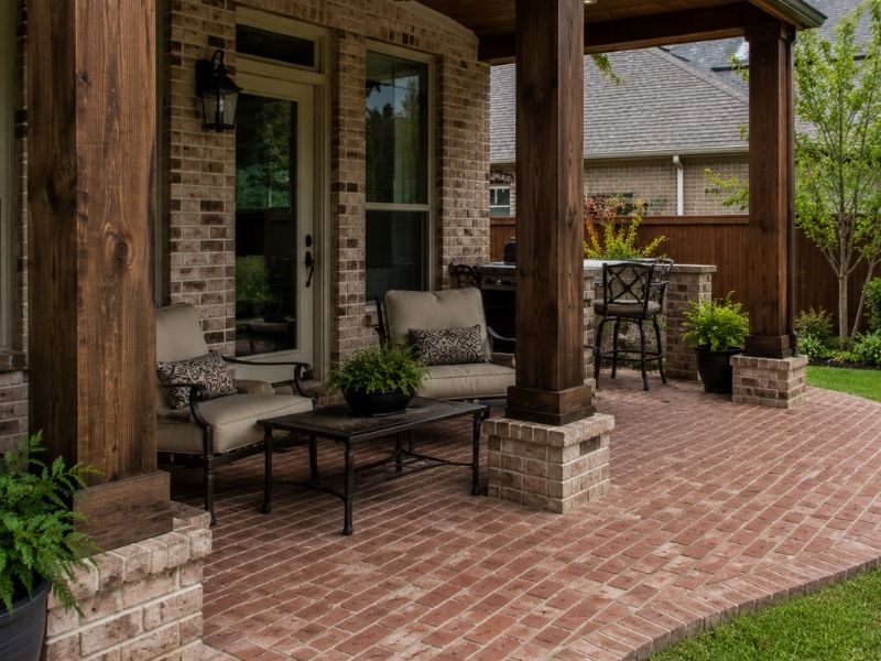Brick patio installation around existing covered porch columns in a residential backyard in Frisco, TX.