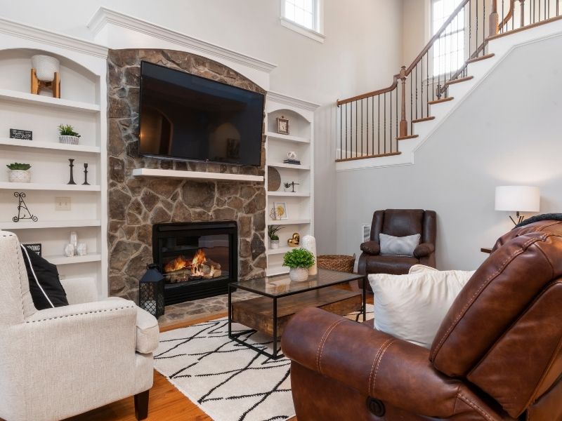 Living room with stone fireplace, mounted TV, and built-in white shelves surrounding the hearth.