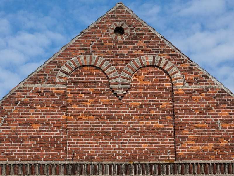 Brick gable wall with two rounded arches and decorative stone voussoirs under a blue sky.