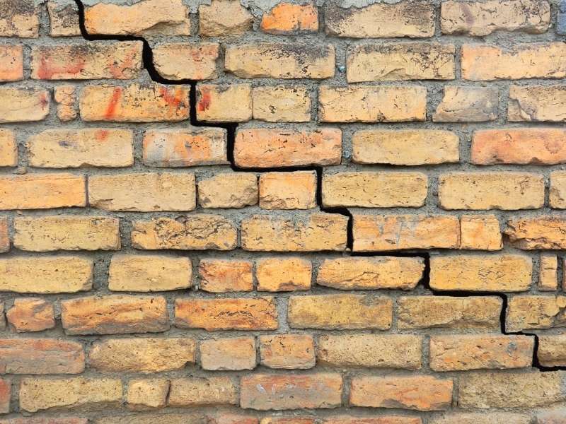 Cracked brick wall with a prominent zigzag fracture running diagonally across,” or “A weathered brick wall split by a bold, irregular vertical crack.