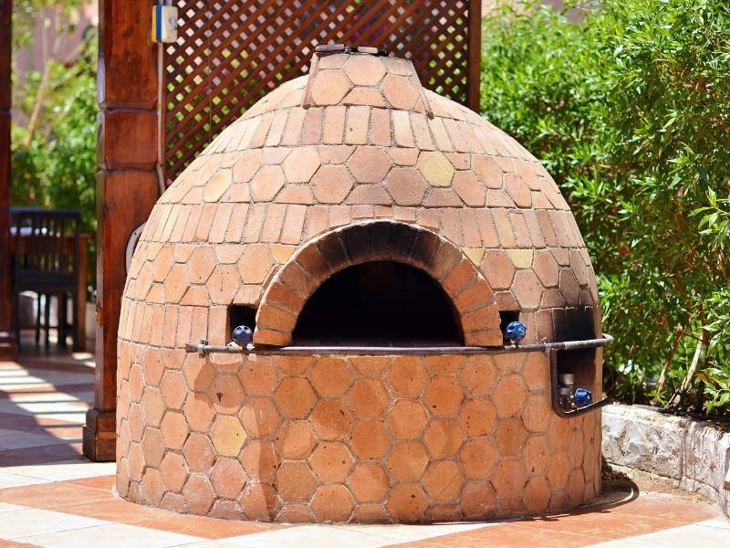 Outdoor brick pizza oven with a domed, hex-tiled exterior and arched opening on a patio.